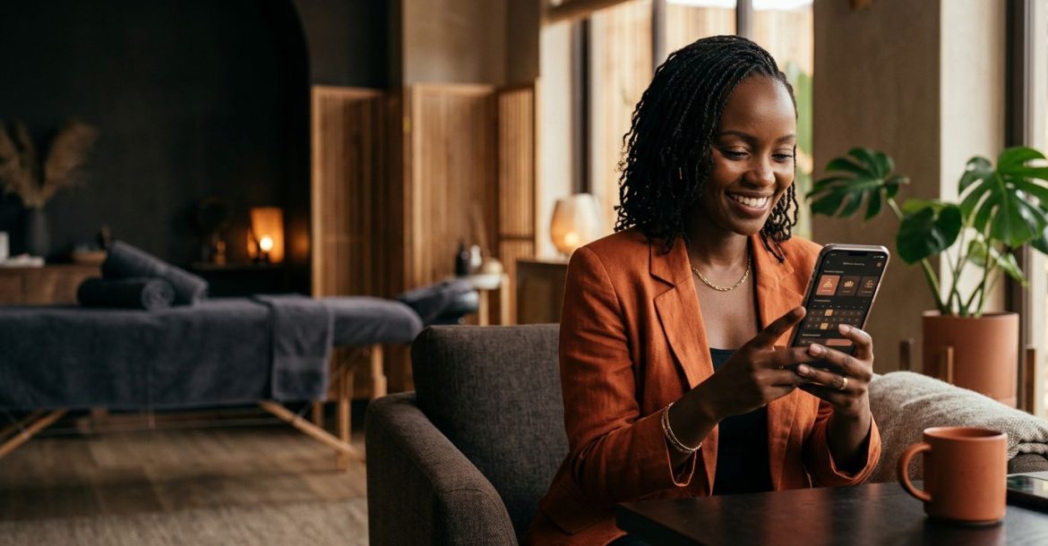 A smiling woman in a Nairobi wellness lounge uses a smartphone app to book a massage.